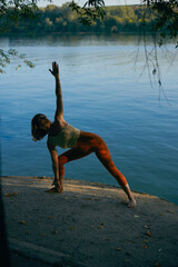 A woman practices yoga pose near the river.