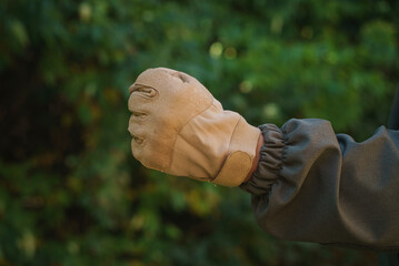 Man arm gesture fists in tactical gloves and deep-green jacket on green forest background.