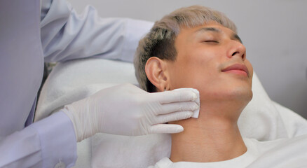 Obraz na płótnie Canvas A handsome Asian man undergoes facial rejuvenation in a beauty clinic using modern medical equipment. By certified beauty experts according to standards.