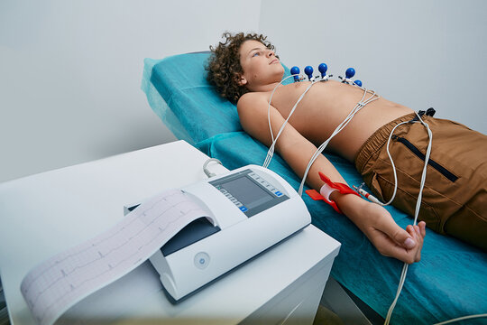 Male Child Lying On Bed During ECG Procedure With Suction Chest Electrodes. Electrocardiography For Children