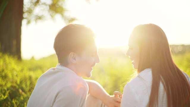 Close-up of loving young couple kissing sitting in wheat field having romantic date on blurred background of bright sunlight. Cheerful man and redhead woman enjoying spending time together in sunset.