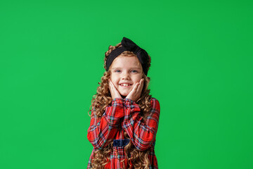 little girl of 7 years old with curly hair and a bow on her head, in a plaid dress, standing and...