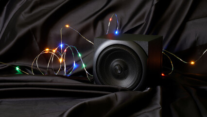 black wooden audio speaker and multi-colored LED garland in a natural silk interior. The concept of festive audio broadcasting and audio streaming. copyspace.