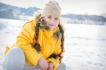Fototapeta na wymiar In winter, on a bright sunny day outside, a little girl in a yellow jacket sat down in the snow..
