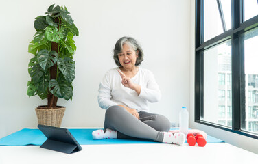 Senior Asian woman watching online courses on a laptop while exercising in the living room at home. Concept of workout training online.