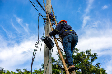 A telecoms worker is shown working from a utility pole ladder while wearing high visibility...