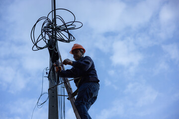 A telecoms worker is shown working from a utility pole ladder while wearing high visibility...