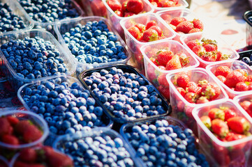 Strawberries and blueberries on a farmer's market stall on a sunny day. Fresh berries are laid out in even rows. Healthy food concept