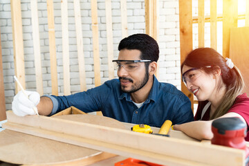 Happy male carpenter and female carpenter working together in the wood workshop. Two asian carpenter working and discuss in the carpentry shop