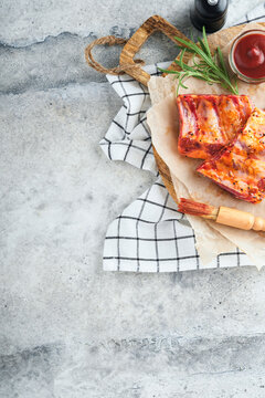 Pork ribs. Raw meat. Raw pork ribs in marinade with spices, rosemary, tomato sauce and garlic on old wooden stand on black stone table background. Barbecue concept. Top view. Mock up.