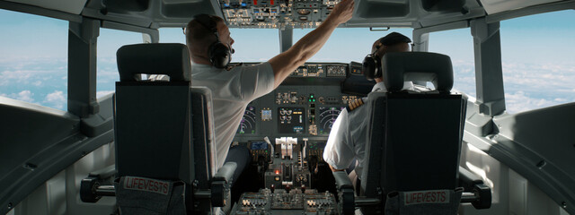 Commercial aircraft pilots adjusting flight parameters of the plane during the flight at high altitude. View from inside the cabin. Real aircraft, daytime shot - obrazy, fototapety, plakaty