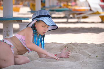 Happy child girl in swimsuit playing with sand under umbrella shadow during summer tropical vacations