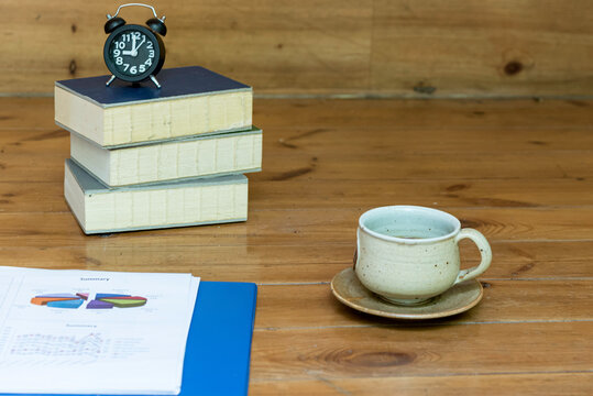 Business report,graph, put on wooden table,cop of coffee,alarm clock and books overlay on left side table. - Powered by Adobe
