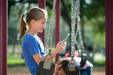 Teen child girl using cellphone sitting on swing in park during summer vacations