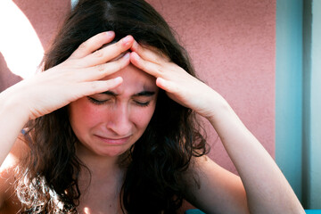 A young caucasion girl is holding her forehead with her hands while crying. Dark, moody.