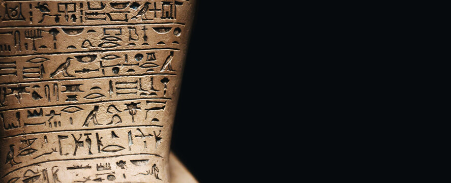 A stone tablet engraved with ancient Egyptian hieroglyphic symbols against a dark black background with copy space - Powered by Adobe