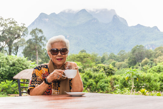 Asin grey white hair senior woman drinking coffee in cafe outdoor with mountain view.