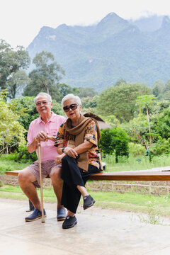 Vertical of asian senior couple sit on a bench on vacation outdoors.