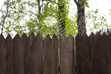 Fototapeta premium wooden fence at the house in the meadow, you can see leaves from the trees behind the fence.