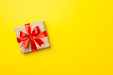Gift box with red ribbon bow on color background, top view