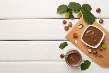 Naklejka na ściany i meble Hazelnut cream with nuts and green leaves on wooden background, top view
