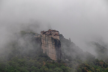 Fototapeta na wymiar Panoramic view of Holy Orthodox Monastery of Rousanou (St. Barbara), Kalambaka, Meteora, Thessaly, Greece, Europe. Unique rock formation are surrounded by mystical fog. Moody dramatic atmosphere