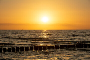 Sunset over the sea, with wooden groynes in the water