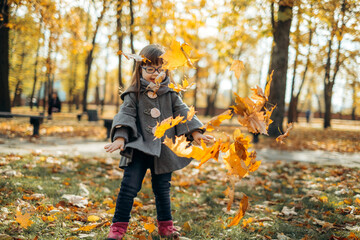 Happy cute brown-haired girl with down syndrome in fashionable coat and stylish eyeglasses tossing...
