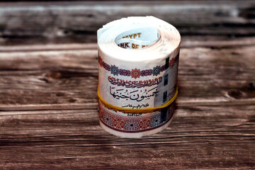 Egypt money roll pounds isolated on wooden background, 50 LE fifty Egyptian pounds cash money bills rolled up with rubber bands with a image of Abu Hurayba Mosque, temple of Edfu and winged scarab - obrazy, fototapety, plakaty