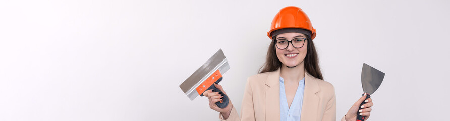 Girl engineer in an orange construction helmet with plastering painting tools in her hands on a white background.