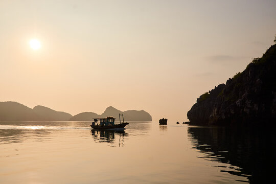 lonely boat in the bay at sunset near the island in the azure sea. beautiful natural background. rocky islands in Vietnam. halong bay
