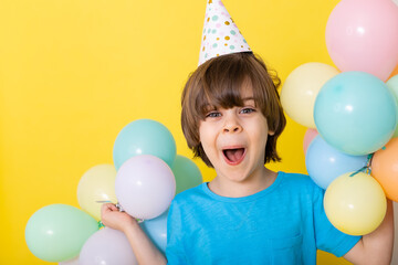 Fototapeta na wymiar Handsome Little birthday boy in blue shirt and hat with balloons, yellow background, happy birthday