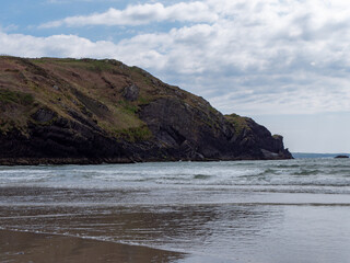 View of the coastal cliffs from the Warren beach. The rocky coast of the south of Ireland. Hills under the sky on a spring day, mountain beside sea, clouds.