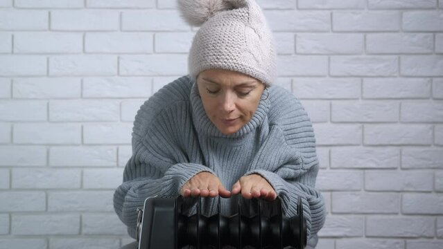 Resting by electric heater. A woman resting and warming by the electric heater in the room. A concept of heating trouble and household debs in Europe.