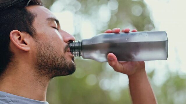 Man drinking water after workout and running outside, being healthy and hydrated. Portrait of male taking a sip of water from bottle after exercise in the park. Fitness, sports and training in nature