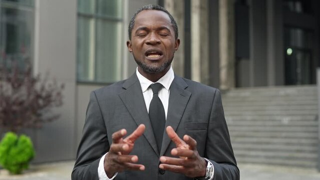 Close up portrait of handsome African American male politician in suit speaking while giving emotional speech to journalists in street. Businessman giving interview outdoor. Public relations concept
