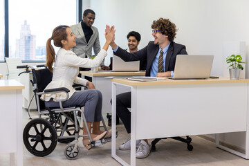 Handicap business woman giving high-five to colleague in creative office. Office workers and woman in a wheelchair are making a conversation in bright office. They are showing a teamwork.