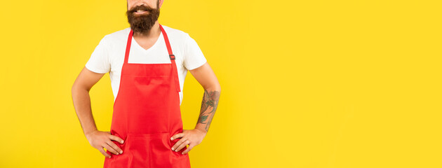 Happy man crop view in red apron keeping arms akimbo yellow background copy space, householding