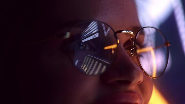 Close up view of woman's eyes in glasses looking at pc screen with computer reflection at eyewear. Using internet, working online, stock rates.