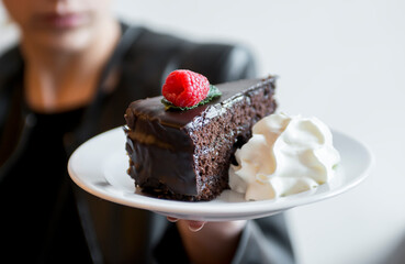 Woman showing chocolate cake with whipped cream, defocused backgroud