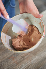 a woman's hand stirs cream in a bowl for decorating a cake with a spatula