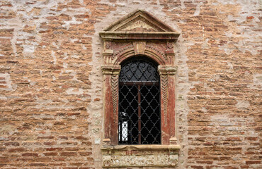 Fototapeta na wymiar An antique orthodox monastery window with wrought iron on an orange brick wall
