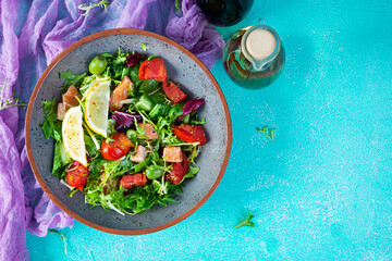 Fresh salad with salmon fish mixed with greens, tomato, olives, mustard and lemon juice