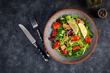 Fresh salad with salmon fish mixed with greens, tomato, olives, mustard and lemon juice