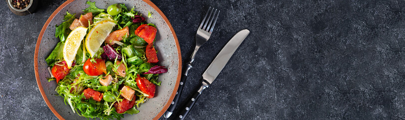 Fresh salad with salmon fish mixed with greens, tomato, olives, mustard and lemon juice