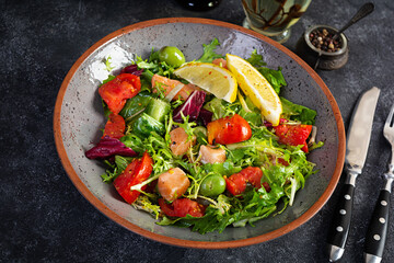 Fresh salad with salmon fish mixed with greens, tomato, olives, mustard and lemon juice