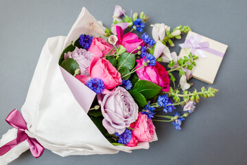 Close up of bouquet of roses foxgloves bachelor buttons flowers wrapped in paper with gift box. Present for holiday