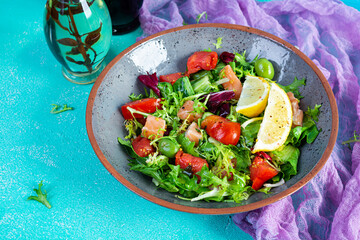 Fresh salad with salmon fish mixed with greens, tomato, olives, mustard and lemon juice