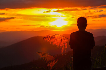 Silhouette of an old man watching beautiful lights during Twilight and watching sunset on mountains alone in loneliness. An old man is traveling and watching view of the setting sun on high mountains.