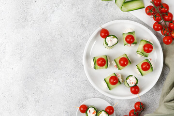 Cucumber rolls stuffed with cream cheese, tomatoes cherry over it, served on a white plate. Holiday...